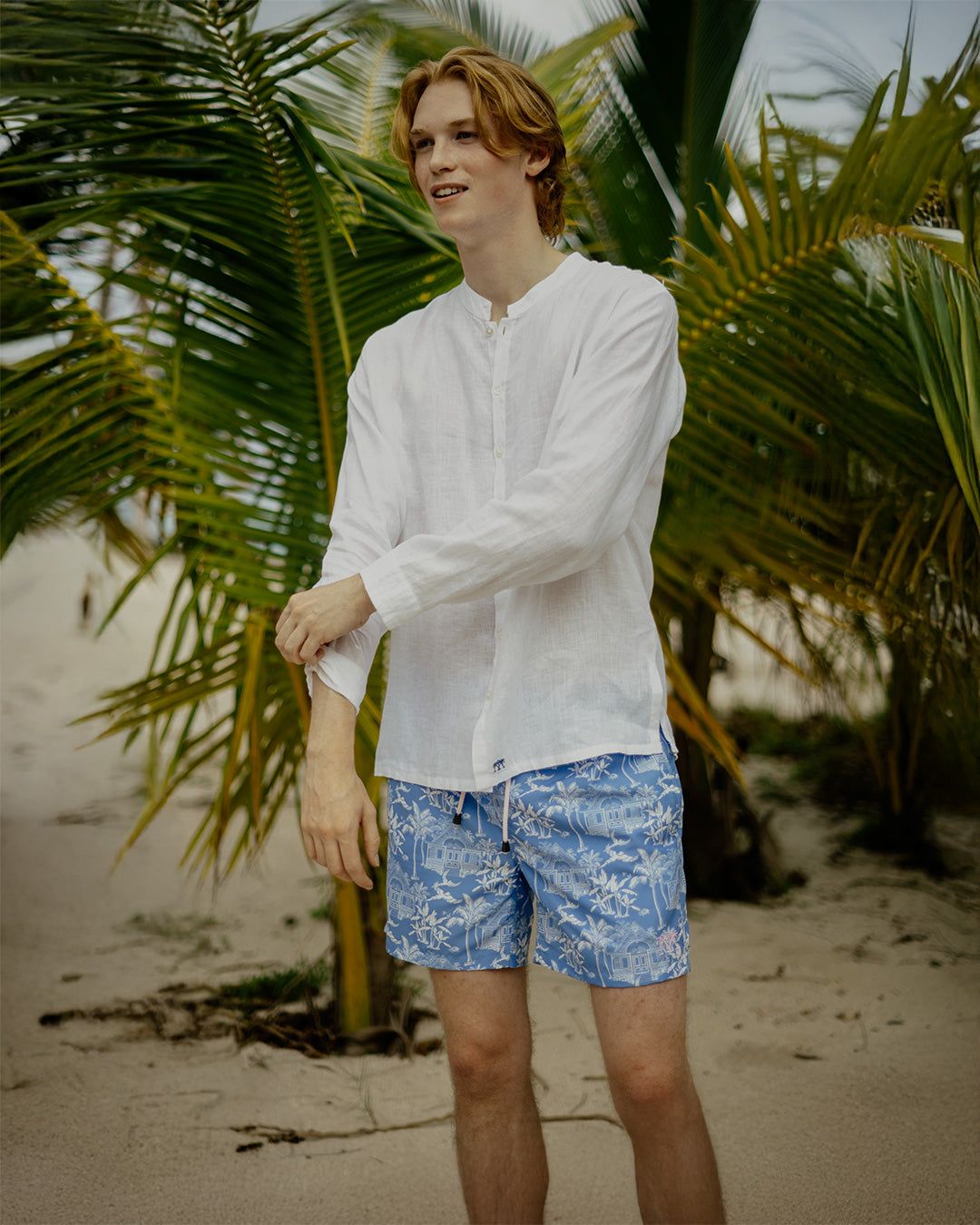 Tropical beach vacation essentials for mens recycled, swim shorts in signature blue Toile de Jouy worn with classic white collarless linen shirt