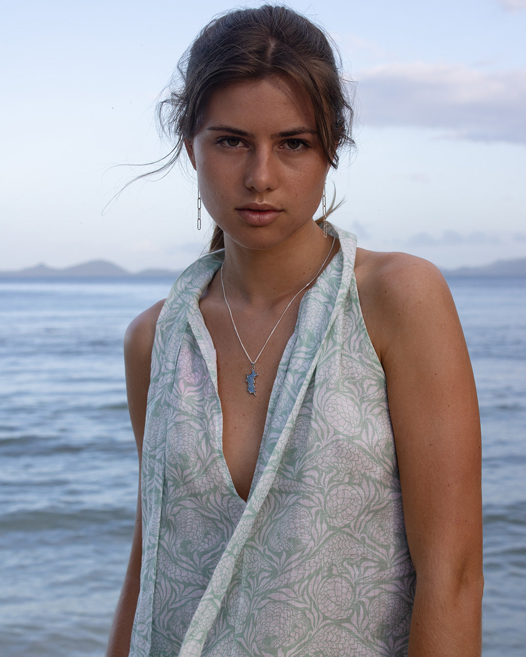 Woman wearing a chic reversible linen beach dress in green Pangolin design in front of the sea, Mustique Island