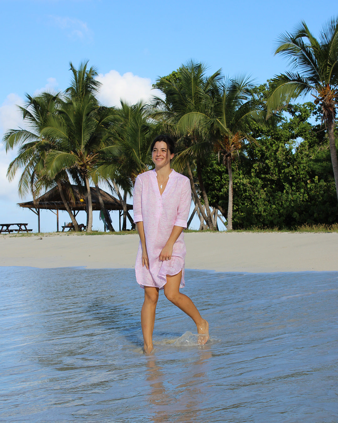 Woman in a pink Pangolin linen Decima dress standing in the tropical waters of Lagoon Bay, Mustique Island