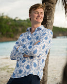 Man leaning against a palm tree on a tropical island in a linen shirt with blue Turtle Trellis design