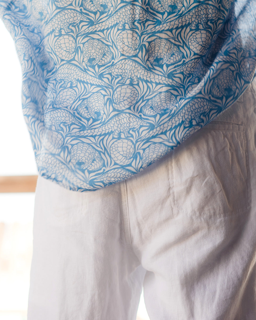 Close up of a quality linen shirt tail in blue Pangolin pattern worn with classic white linen shorts for luxury island vacation style