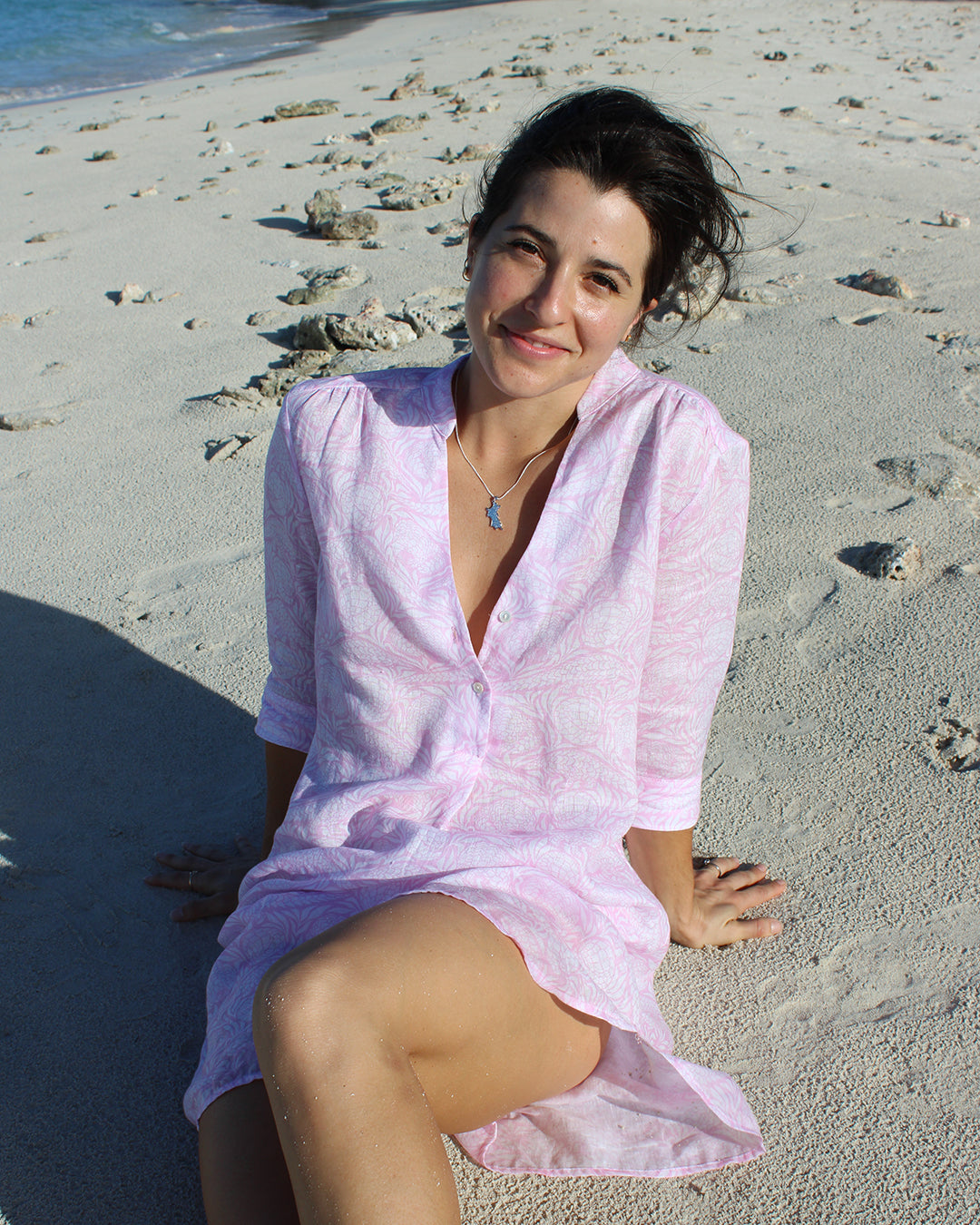 Woman sitting on the beach in a pink Pangolin linen Decima dress Lagoon Bay, Mustique Island